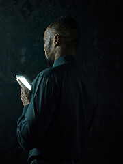 Image showing Studio shot of young serious black African man thinking while talking on mobile phone against black background