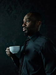 Image showing Stylish young black man with cup of coffee posing on dark background.