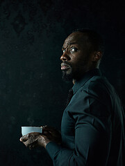 Image showing Stylish young black man with cup of coffee posing on dark background.