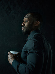 Image showing Stylish young black man with cup of coffee posing on dark background.