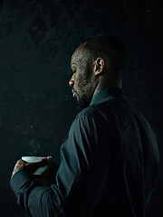 Image showing Stylish young black man with cup of coffee posing on dark background.