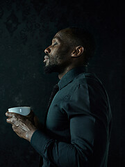 Image showing Stylish young black man with cup of coffee posing on dark background.