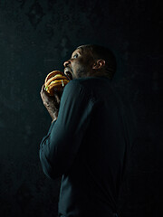 Image showing young african american man eating hamburger and looking away on black studio