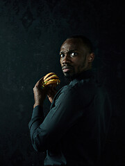 Image showing young african american man eating hamburger and looking away on black studio