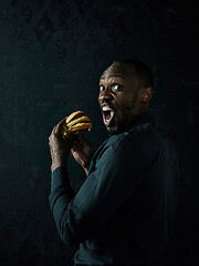 Image showing young african american man eating hamburger and looking away on black studio