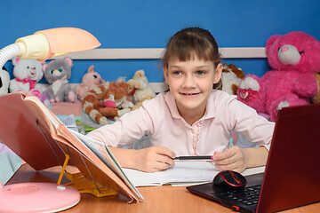 Image showing The girl in the children\'s room sits at the desk with a smile and does her homework