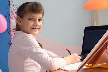 Image showing Girl in good spirits doing homework at the desk at home