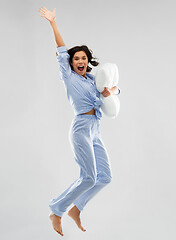 Image showing happy woman in blue pajama jumping with pillow