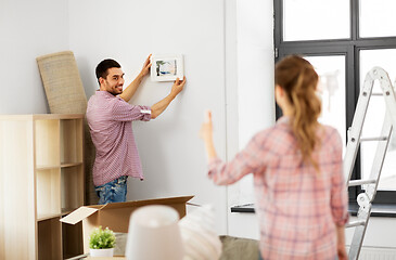 Image showing happy couple moving to new home and hanging photo