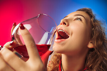 Image showing The surprised young woman in party clothes posing with glass of wine.