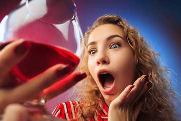 Image showing The surprised young woman in party clothes posing with glass of wine.