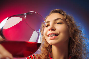 Image showing The surprised young woman in party clothes posing with glass of wine.