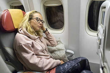 Image showing Tired blonde casual caucasian lady napping on uncomfortable seat while traveling by airplane. Commercial transportation by planes.