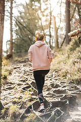 Image showing Rear view of active sporty woman listening to the music while running in autumn fall forest. Female runner training outdoor. Healthy lifestyle image of young caucasian woman jogging outside