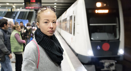 Image showing Young woman in winter coat going to work, waiting on the platform of a railway station for train to arrive. Public transport