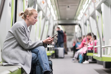 Image showing Portrait of lovely girl typing message on mobile phone in almost empty public subway train. Staying at home and social distncing recomented due to corona virus pandemic outbreak