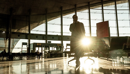 Image showing Silhouette of woman stucked at airport terminal over flight cancellation,calling family, sitting in almost empty airport terminal due to coronavirus pandemic, Covid 19, outbreak travel restrictions