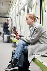 Image showing Portrait of lovely girl typing message on mobile phone in almost empty public subway train. Staying at home and social distncing recomented due to corona virus pandemic outbreak