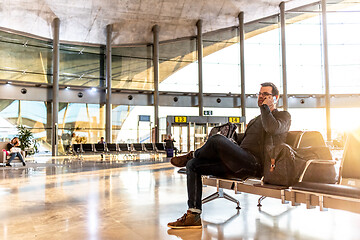 Image showing Casual young male using her cell phone while waiting to board a plane at airport departure gates.