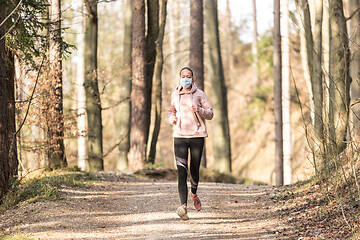 Image showing Corona virus, or Covid-19, is spreading all over the world. Portrait of caucasian sporty woman wearing a medical protection face mask while running in nature.