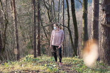 Image showing Corona virus, or Covid-19, is spreading all over the world. Portrait of caucasian sporty woman wearing a medical protection face mask while walking in the forest. Corona virus.