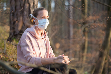 Image showing Portrait of caucasian sporty woman wearing medical protection face mask while relaxing in nature and listening to music. Corona virus, or Covid-19, is spreading all over the world