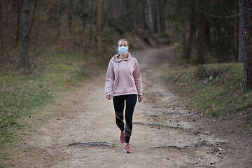 Image showing Corona virus, or Covid-19, is spreading all over the world. Portrait of caucasian sporty woman wearing a medical protection face mask while walking in the forest. Corona virus.