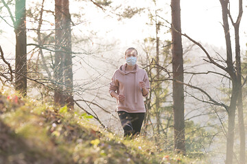 Image showing Corona virus, or Covid-19, is spreading all over the world. Portrait of caucasian sporty woman wearing a medical protection face mask while running in nature.