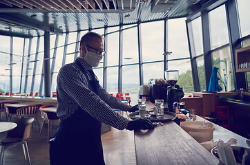 Image showing waiter in a medical protective mask serves  the coffee in restau