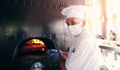 Image showing chef  with protective coronavirus face mask preparing pizza