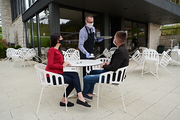 Image showing Waiter with protective medical mask and gloves serving guest