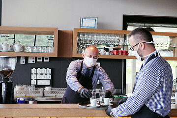 Image showing waiter in a medical protective mask serves  the coffee in restau