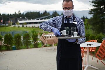 Image showing waiter in a medical protective mask serves  the coffee in restau