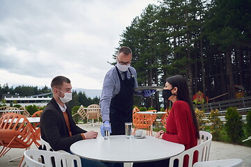 Image showing Waiter with protective medical mask and gloves serving guest