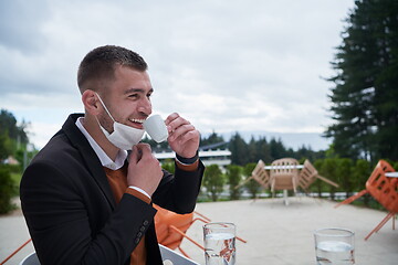 Image showing funny man in restaurant drinking coffee wearing face mask