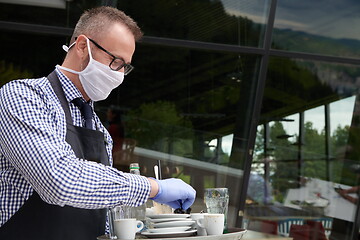 Image showing waiter in a medical protective mask serves  the coffee in restau