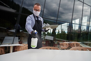 Image showing Waiter cleaning the table with Disinfectant Spray in a restauran