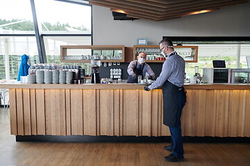 Image showing waiter in a medical protective mask serves  the coffee in restau