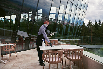 Image showing Waiter cleaning the table with Disinfectant Spray in a restauran
