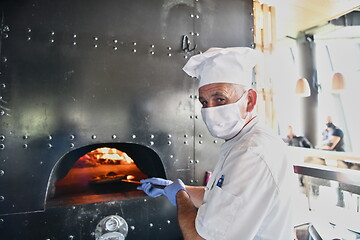 Image showing chef  with protective coronavirus face mask preparing pizza