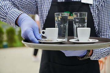 Image showing waiter in a medical protective mask serves  the coffee in restau