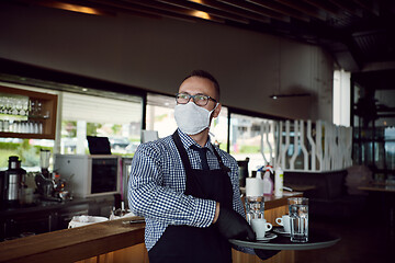 Image showing waiter in a medical protective mask serves  the coffee in restau