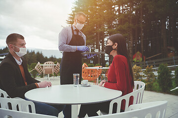 Image showing Waiter with protective medical mask and gloves serving guest