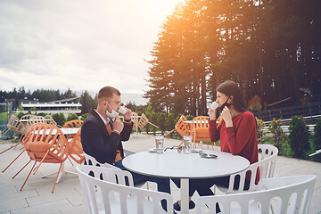 Image showing couple with protective medical mask  having coffee break in a re