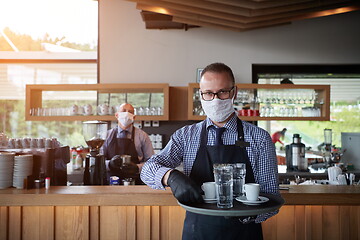 Image showing waiter in a medical protective mask serves  the coffee in restau