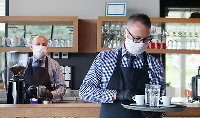 Image showing waiter in a medical protective mask serves  the coffee in restau