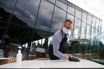 Image showing Waiter cleaning the table with Disinfectant Spray in a restauran