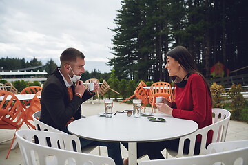 Image showing couple with protective medical mask  having coffee break in a re