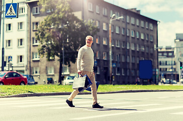 Image showing senior man with shopping bags walking on crosswalk