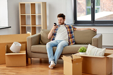Image showing man with smartphone and boxes on sofa at new home